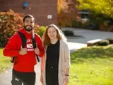 A young man and woman stand on campus and smile